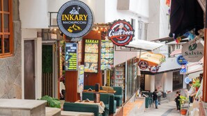 Uma rua estreita com mesas ao ar livre, um letreiro de cerveja artesanal e um cardápio de pizza.