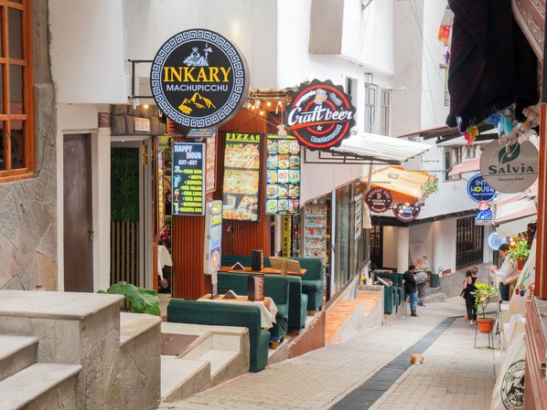 A narrow street with outdoor seating, a craft beer sign, and a pizza menu. - Inkary Hotel Machupicchu  (Machu Picchu)
