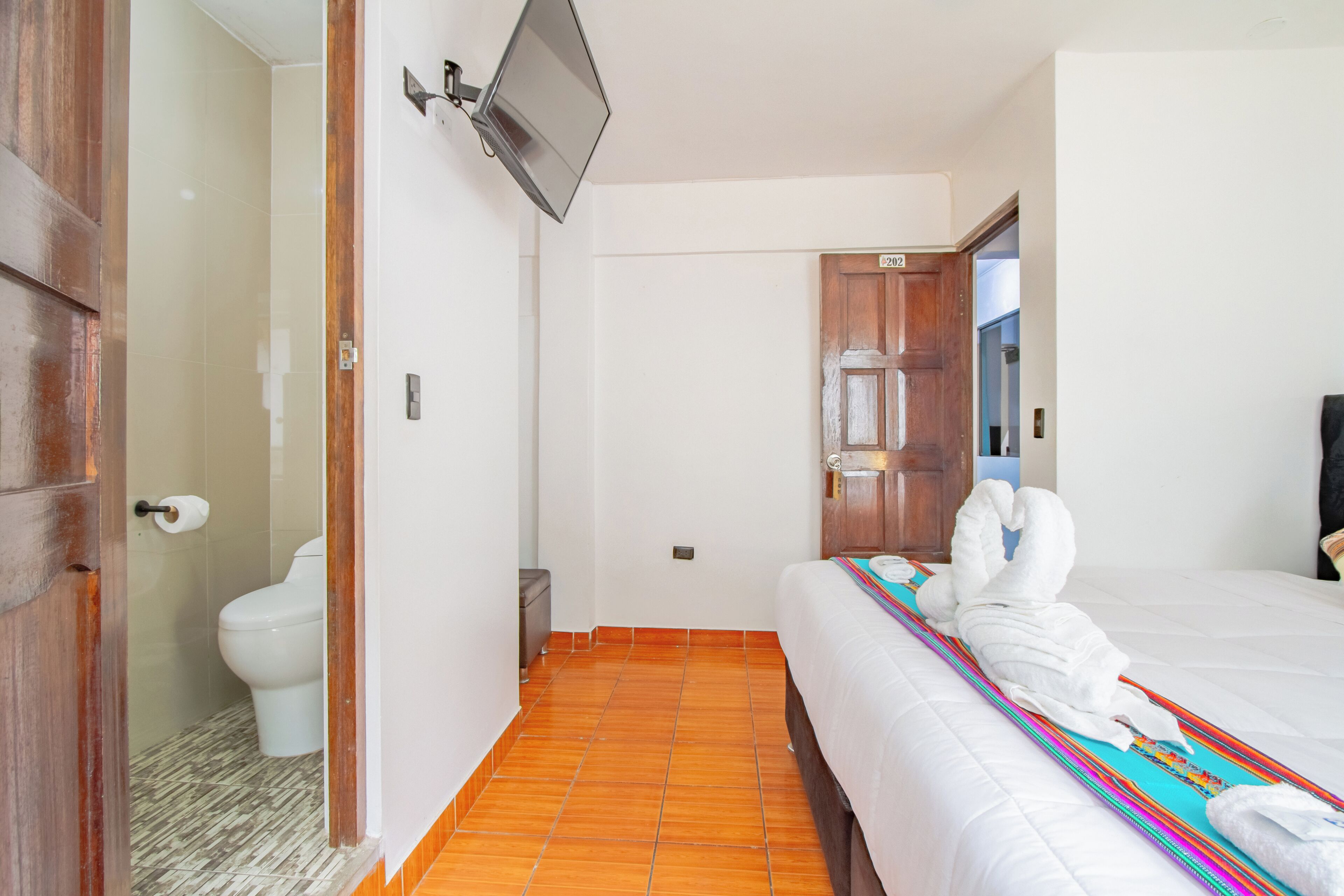 Ein Hotelzimmer mit Bett, Wandfernseher, Toilette und Duschbereich.