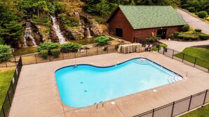 Une piscine avec un chalet en bois et une cascade en arrière-plan.