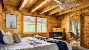 Une chambre confortable, aménagée dans un chalet en bois, avec un lit, une cheminée et un ventilateur de plafond.