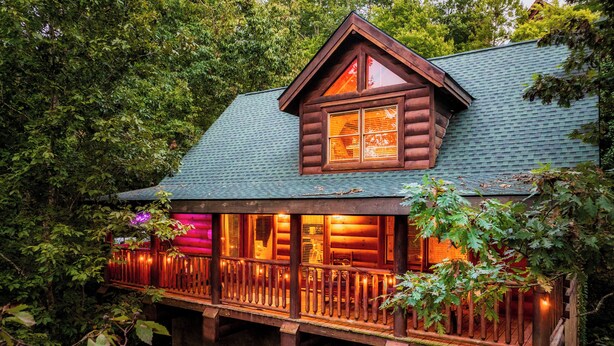 Une cabane en rondins avec une terrasse en bois et une grande fenêtre.