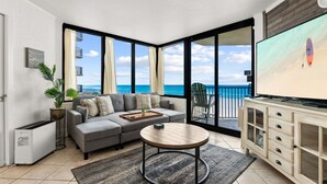 A modern living room with a gray sofa, a round coffee table, and a TV on a wooden cabinet. - Beachfront 2BR! · Sunbird 3rd Floor! Free Beach Chairs & Umbrella Service! (Panama City Beach)