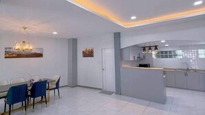 A modern kitchen with a central island, recessed ceiling lights, and a dining area with a table and chairs. - Anjia Serene Pool Villa (Pattaya)