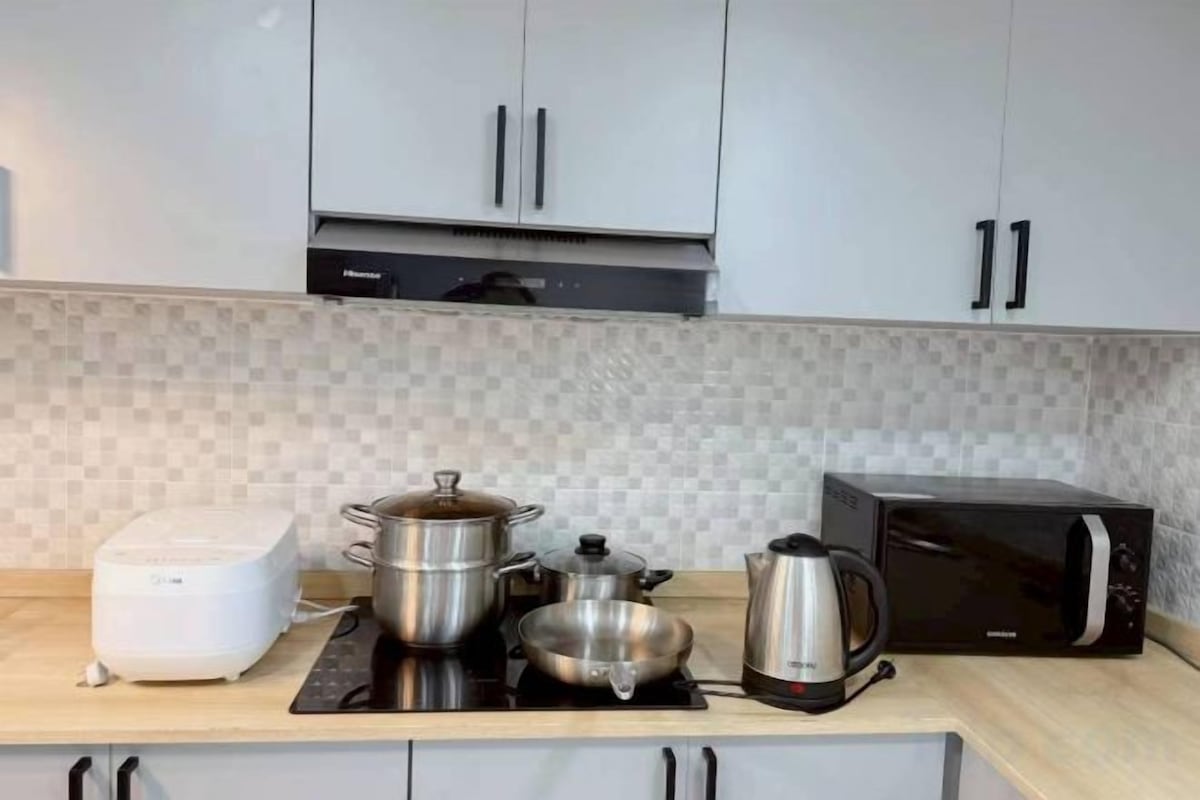 Una cocina con microondas, tostadora, hervidor y una olla sobre una placa de inducción.
