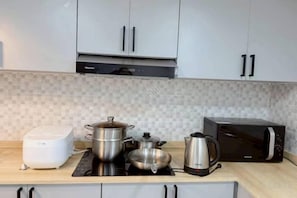 Una cocina con microondas, tostadora, hervidor y una olla sobre una placa de inducción.