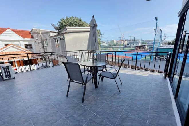 Un balcón con mesa y sillas, una piscina al fondo y un edificio de techo rojo.
