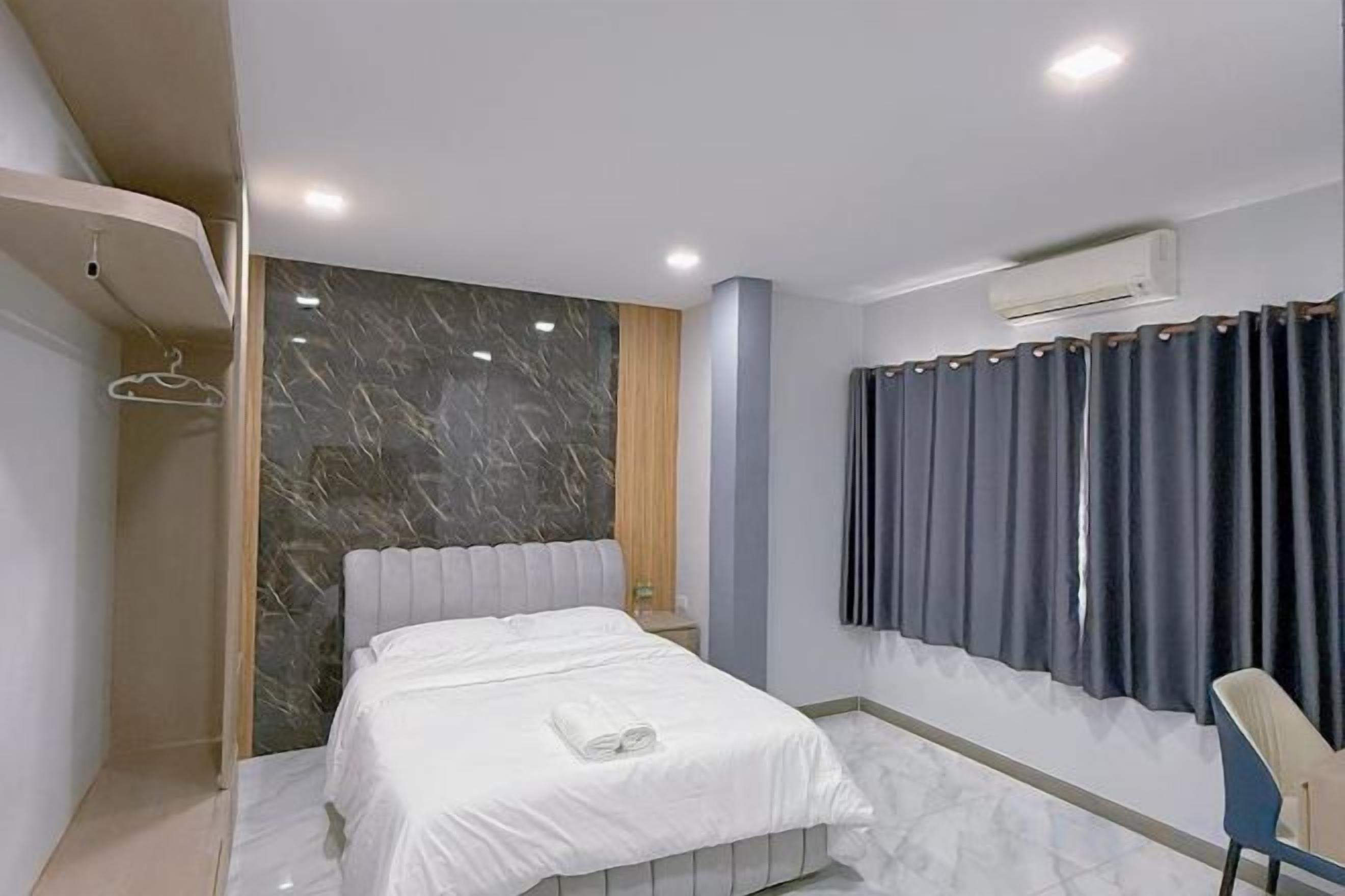 A modern hotel room with a marble accent wall, a bed with white linens, a shower area, and a window with curtains.