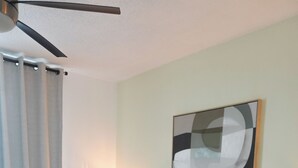 Un lit bien fait, agrémenté d’oreillers à rayures, une lampe de chevet et un ventilateur de plafond dans une chambre d’hôtel.