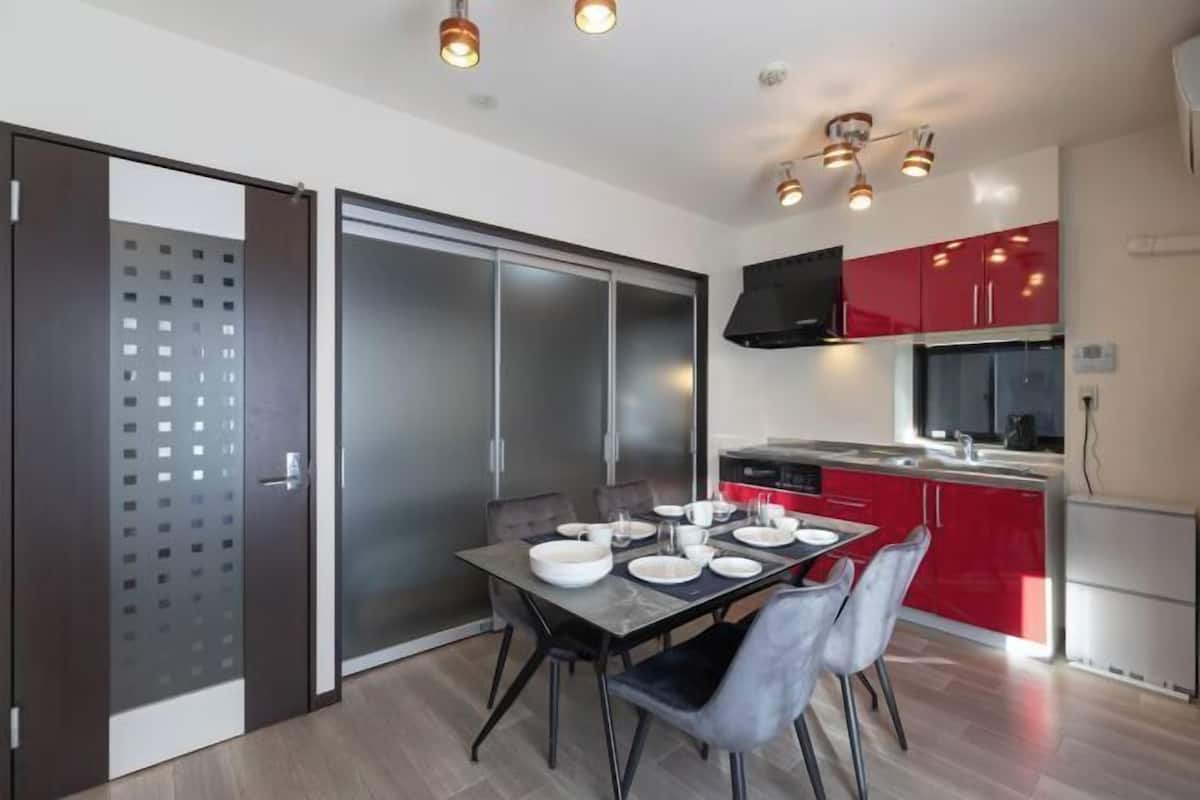 A modern kitchen with red cabinets, a dining table set for four, and a sliding glass door closet.