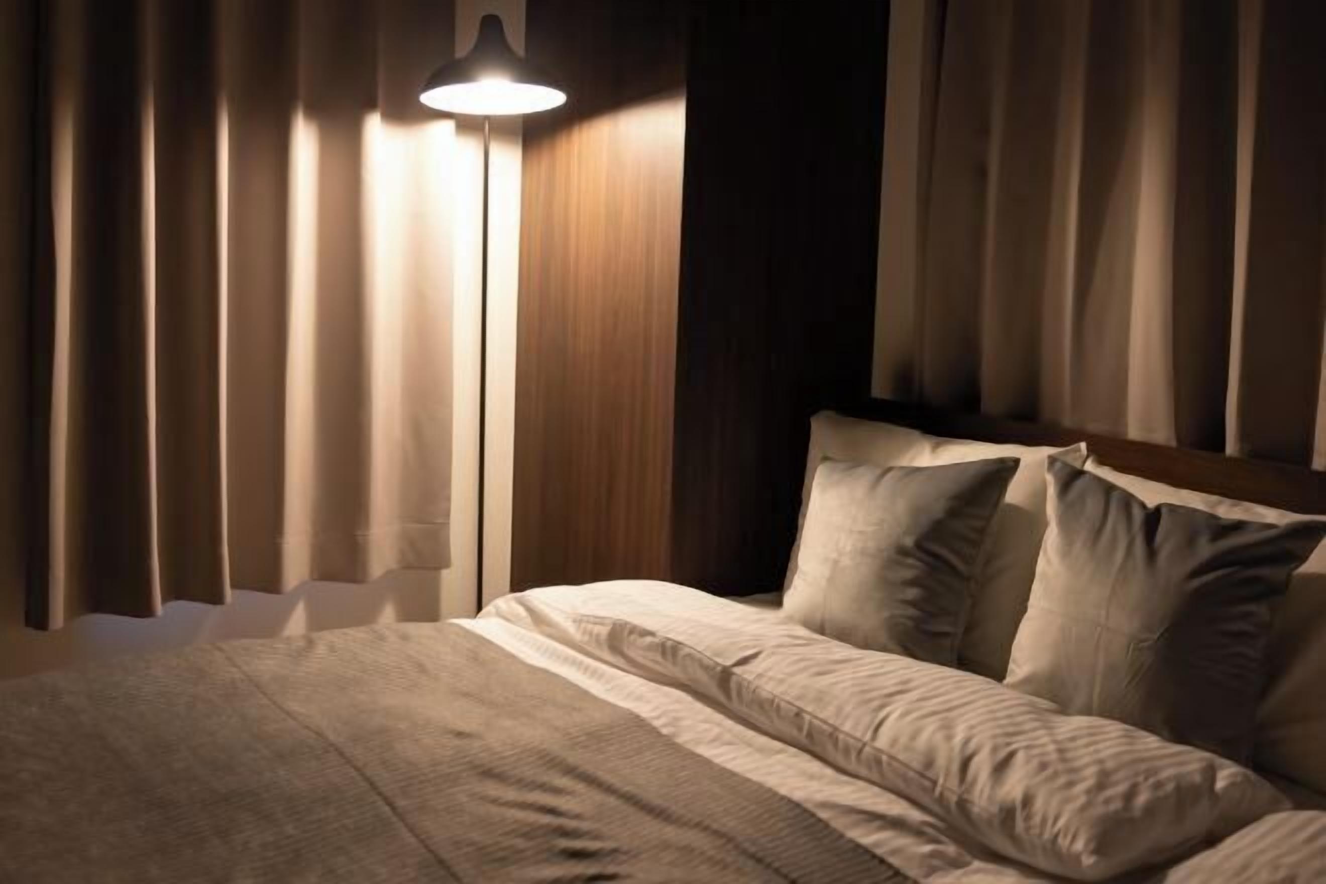 Un lit bien fait, avec une couverture à rayures et des oreillers, une lampe sur pied et des rideaux.