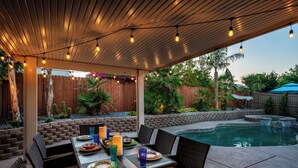 An outdoor patio with a pool, dining area, and covered seating. - Welcome to Villa Tempo - Pool, Spa, Game Room, BBQ, Fast Wifi, Sleeps 12+ (Coachella)