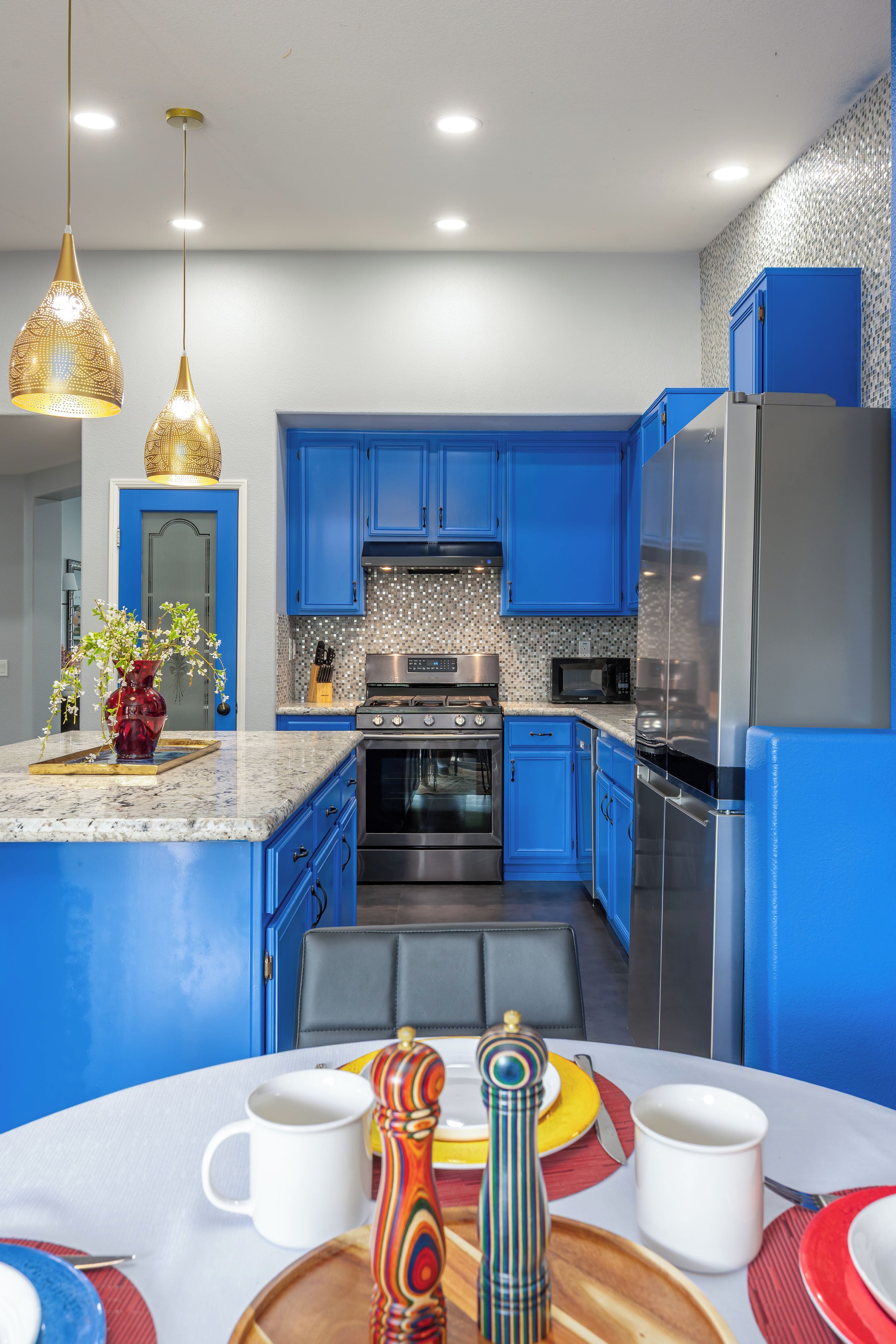 A modern kitchen with blue cabinets, stainless steel appliances, and a marble countertop.