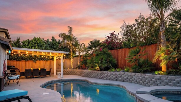 A backyard with a swimming pool, a barbecue area, and a covered seating area with string lights. - Welcome to Villa Tempo - Pool, Spa, Game Room, BBQ, Fast Wifi, Sleeps 12+ (Coachella)