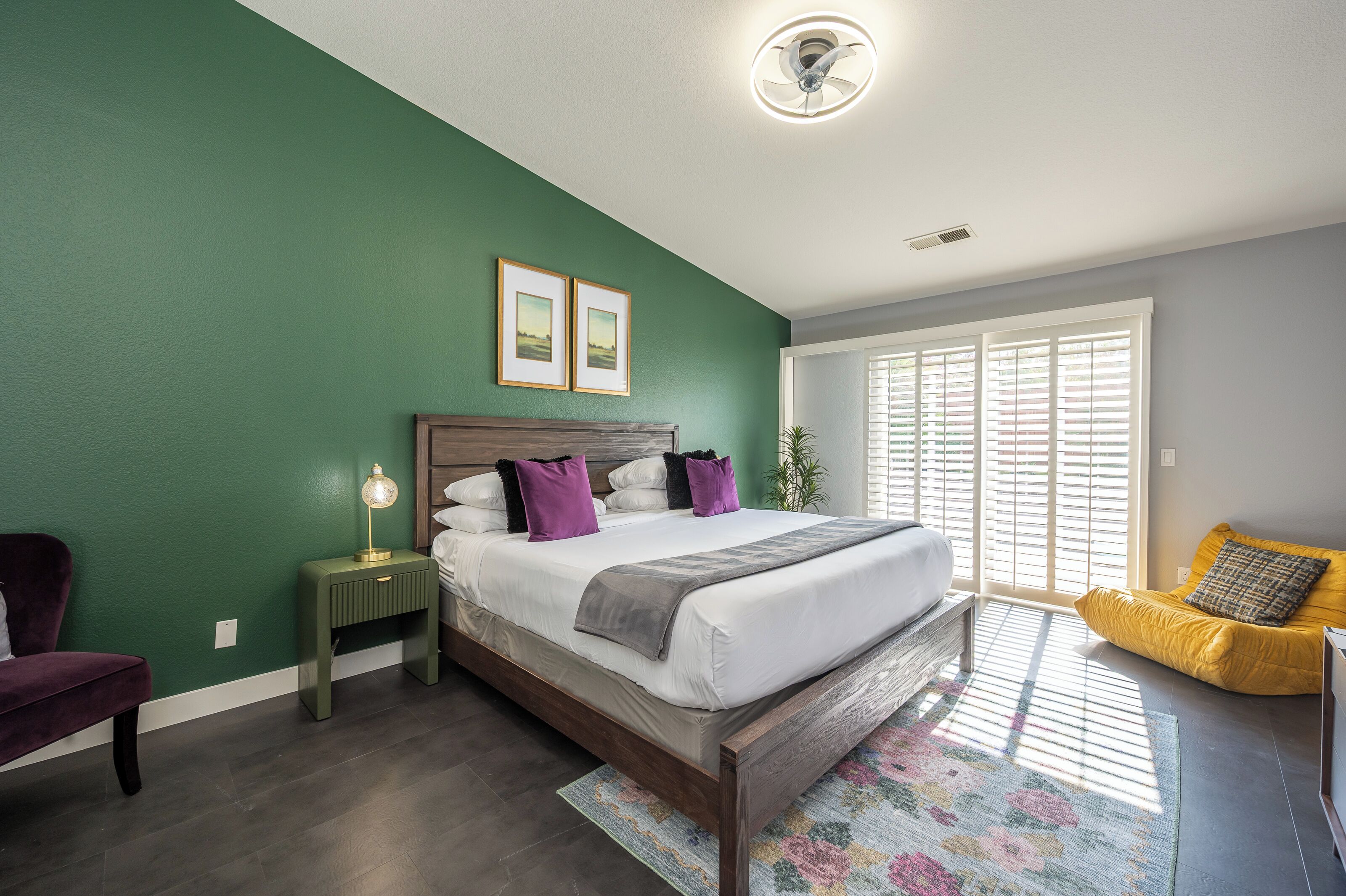A bedroom with a bed, a nightstand, a chair, and a window with blinds.