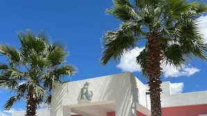 A building with a white facade and a pink entrance. There are palm trees and potted plants in front. - Rosa y Oro Hotel Boutique (Jesús María)