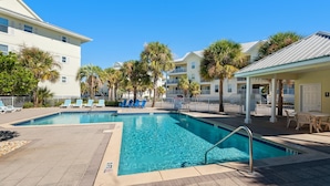 A swimming pool with lounge chairs and palm trees, surrounded by buildings with balconies. - Gulf Island 232 - Sunset Suite (Navarre)