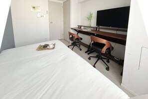 A hotel room with a bed, a desk, two chairs, a television, and a small plant.