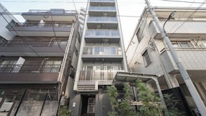 A multi-story residential building with balconies, a central entrance, and a small garden area.