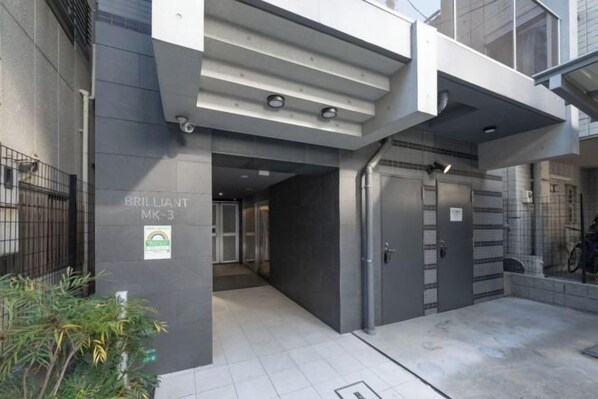 Una entrada moderna de edificio con una reja metálica, un letrero que indica 'BRILLIANT MK-3' y un suelo de baldosas.