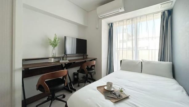 A hotel room with a bed, a desk with a chair, a TV, and an air conditioning unit.