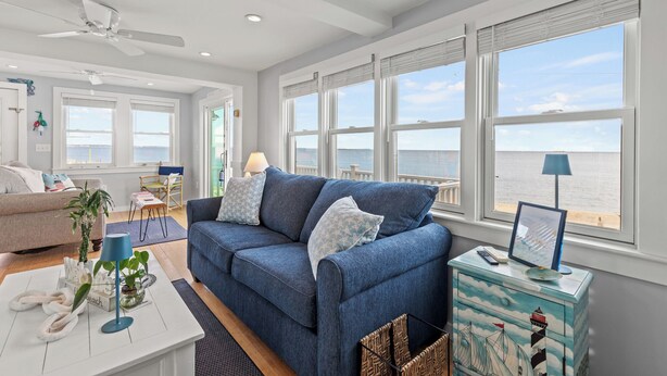 A spacious living room with a large window overlooking the sea, a blue sofa, a white coffee table, and a decorative cabinet.
