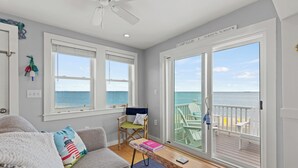 A room with a view of the ocean, a ceiling fan, a couch, a chair, and a table with books.
