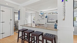 A modern kitchen with a central island, bar stools, and a 'WELCOME' sign.