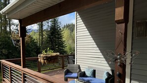 A wooden deck with wicker furniture and a hanging planter. - Bear Bottoms at Salmon Creek (Seward)