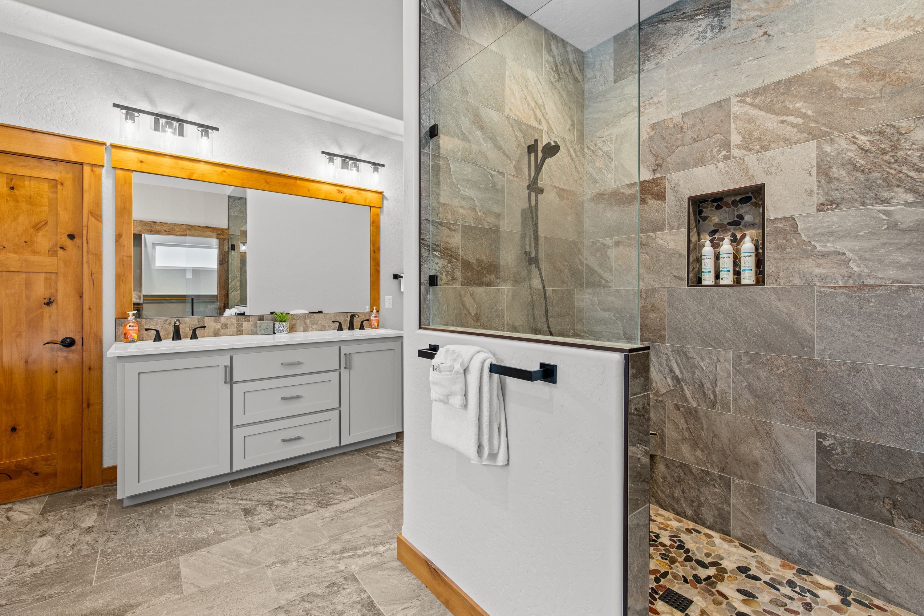 A modern bathroom with a large mirror, a shower with a stone wall, and a vanity with a towel rack.