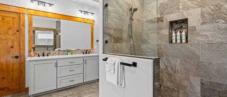 A modern bathroom with a large mirror, a shower with a stone wall, and a vanity with a towel rack.