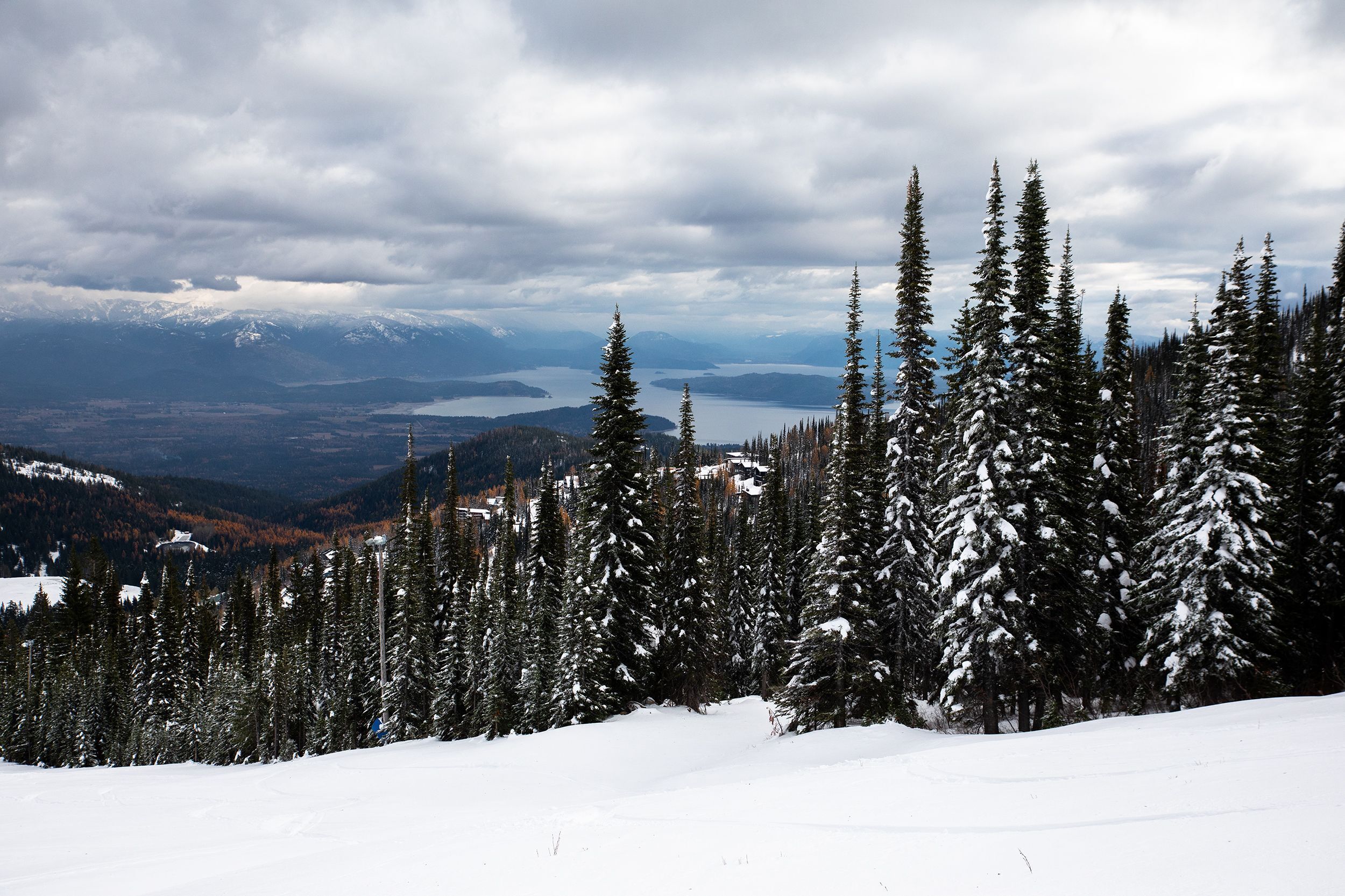 Paisagem coberta de neve, com vista para montanhas distantes e um lago.