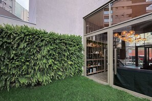Un edificio moderno con un amplio ventanal, un seto verde y una lámpara colgante.
