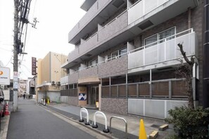 A multi-story building with a commercial ground floor, a parking lot, and a street with traffic cones. - Sharman Yayoi (Tokyo)