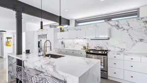 A modern kitchen with a marble island, stainless steel appliances, and pendant lighting. - Modern West PS - Welcome to Paradise! (Palm Springs)