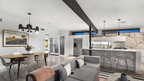 A modern living room with a grey sofa, dining area, and kitchen with marble countertops. - Modern West PS - Welcome to Paradise! (Palm Springs)