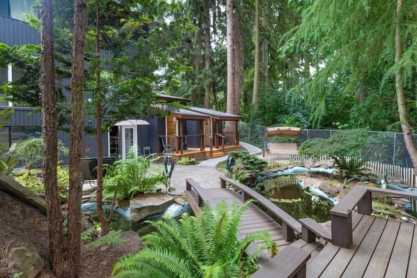 Une terrasse en bois avec un petit étang, entourée de fougères et d’arbres.