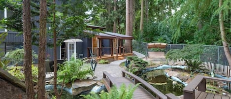Une terrasse en bois avec un petit étang, entourée de fougères et d’arbres.
