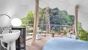 Une chambre avec un grand lit, un lavabo, un miroir et une vue sur une forêt grâce à un mur en verre.