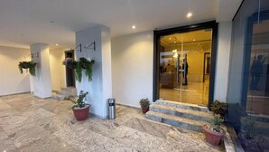 Vestíbulo de hotel con suelo de mármol, plantas en macetas, una mesa de recepción y entrada de vidrio.