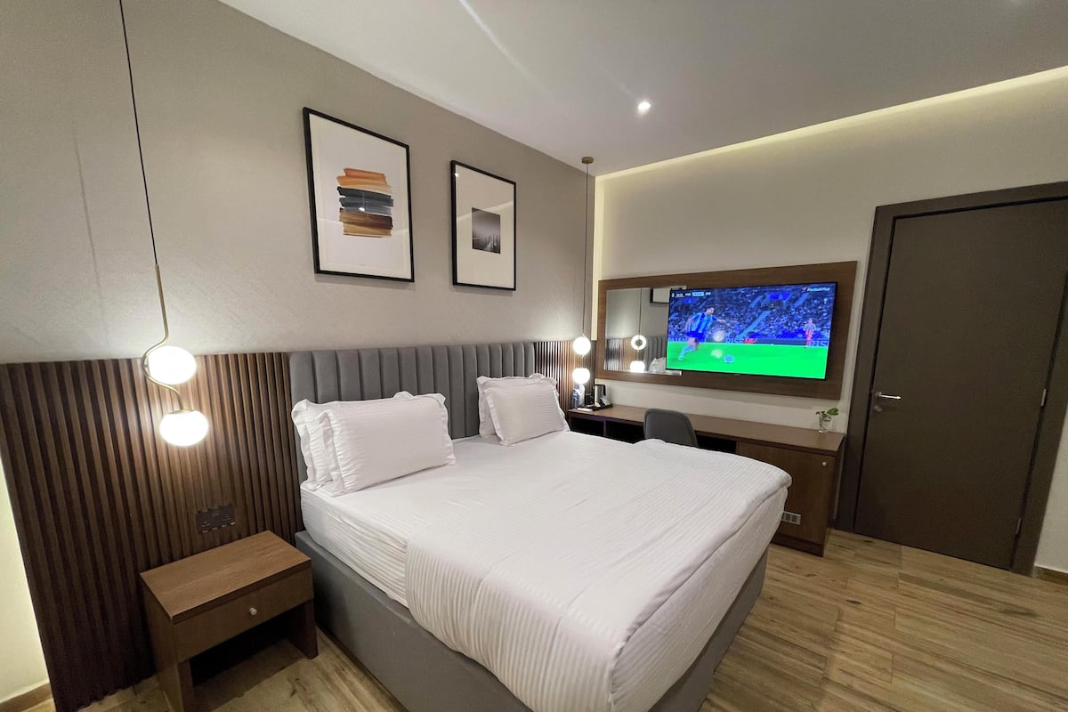 Une chambre d’hôtel moderne avec un grand lit, des tables de chevet, un bureau, une télévision et un miroir.