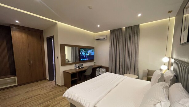 Una habitación de hotel moderna con una cama grande, un escritorio con ordenador, un televisor y un armario.