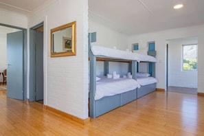 A room with bunk beds, a wooden floor, white walls, and a mirror.