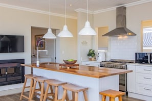 A modern kitchen with a central island, bar stools, pendant lights, a stove, and a TV.