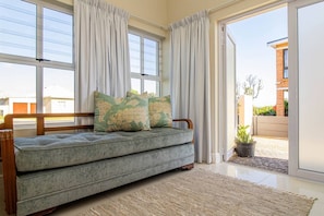 A modern living room with a grey sofa, two decorative pillows, a wooden bench, and a large window with white curtains.