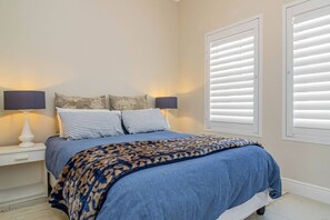 Un dormitorio con cama, dos mesitas de noche, lámparas y una ventana con persianas.