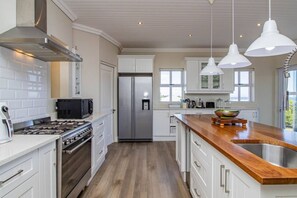 A modern kitchen with white cabinetry, stainless steel appliances, a wooden countertop, and pendant lighting. - Salt & Sea | Near beaches | Ocean view (Sandbaai)