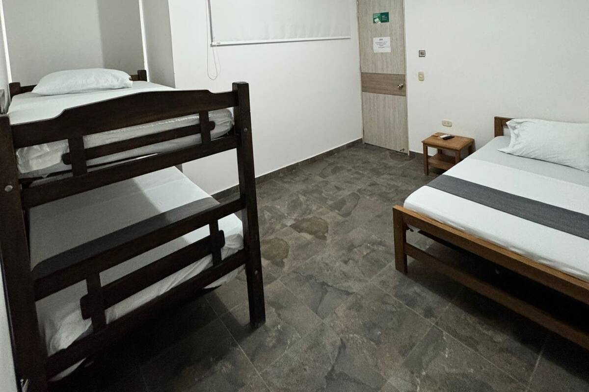 A room with two bunk beds, a small wooden table, a whiteboard, and a door with a light switch.