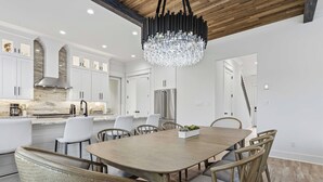 Una cocina moderna con gabinetes blancos, una isla grande, electrodomésticos de acero inoxidable y una araña.