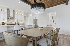 A modern kitchen with white cabinets, a large island, stainless steel appliances, and a chandelier.